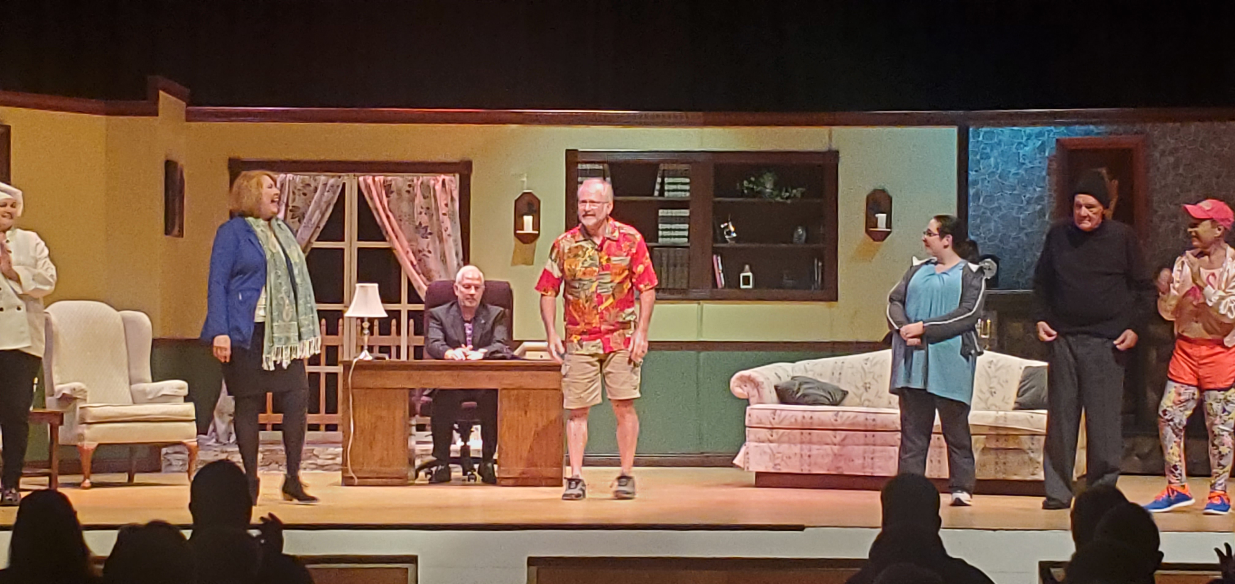 From left to right: a chef in a tope; a woman in a blue jacket and light green scarf; a man in a black suit sitting behind a desk; a man in a red Hawaiian shirt and brown shorts; a woman in a long bluish green top;
       a man in a black pullover, gray pants and black cap; and a man in an orange running outfit.