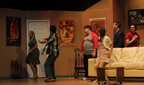 A man tries to stop a woman in a green dress from leaving while a man in a Buccaners T-shirt, a young woman, a man in a suit, and a
       man in a red Avengers T-shirt look on
