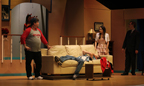 A man lies on the couch covering his face, while a man in a Buccaneers T-shirt and a young woman stand at either end
      and a man in a suit looks on