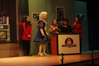 The man in the wig and white and blue sparkly skirt, the woman in the gold Starfleet uniform sitting at a console, the woman in the black sparkly skirt sitting
       at a console, with two women in red Starfleet uniforms on either side 