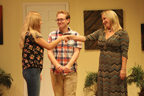 A young woman in jeans and sandals shakes hands with the woman in a horizontally
       striped long dress, with a young man in a plaid shirt behind them